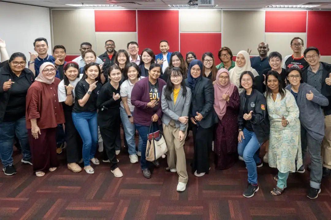 A large group of smiling advisors and trainers giving thumbs up together in a training room after a full-day AI training session in Klang, 9 October 2026